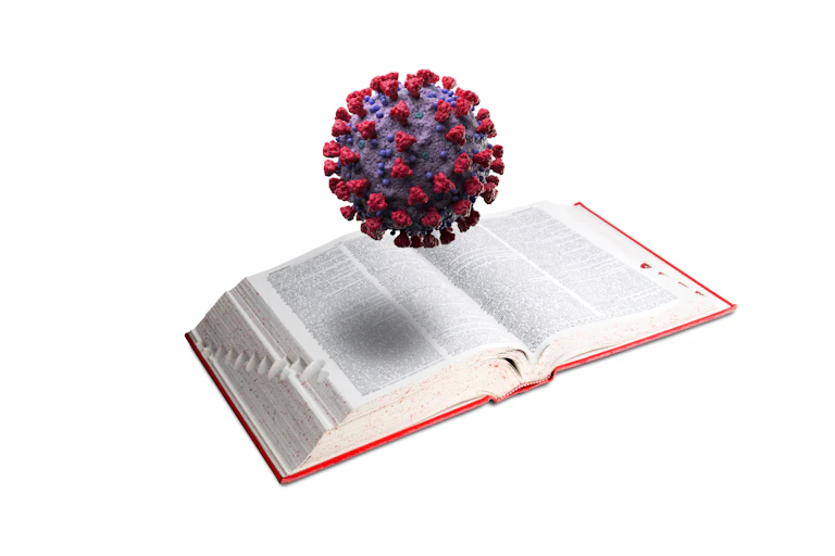 A 3D model of the coronavirus hovers over an open dictionary.