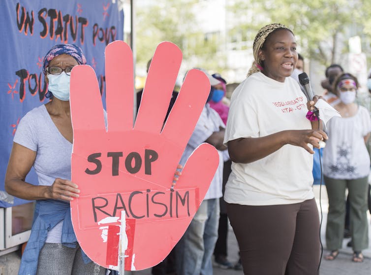 People demonstrate, with one holding up a sign that says Stop Racism.