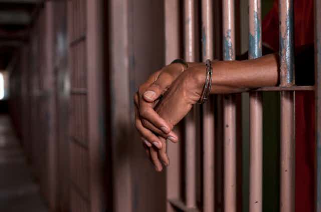 A Black man's hands extend out from inside prison bars. 
