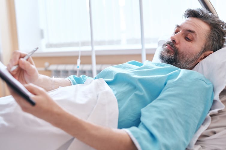 Man lying down in hospital bed signing papers