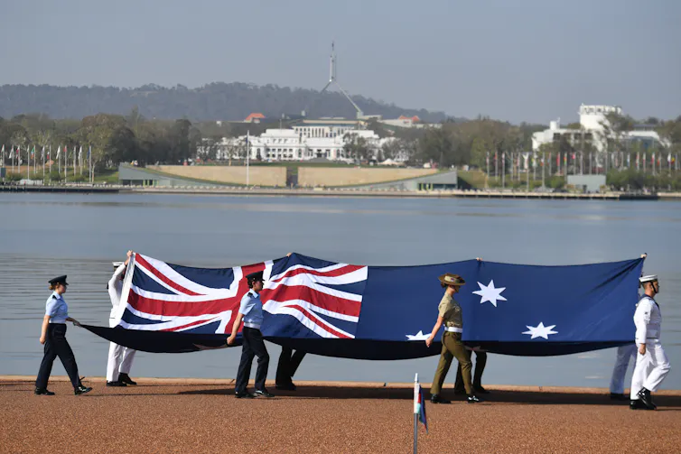 Armed forces members carry a large Australian flag with Parliament House in the background