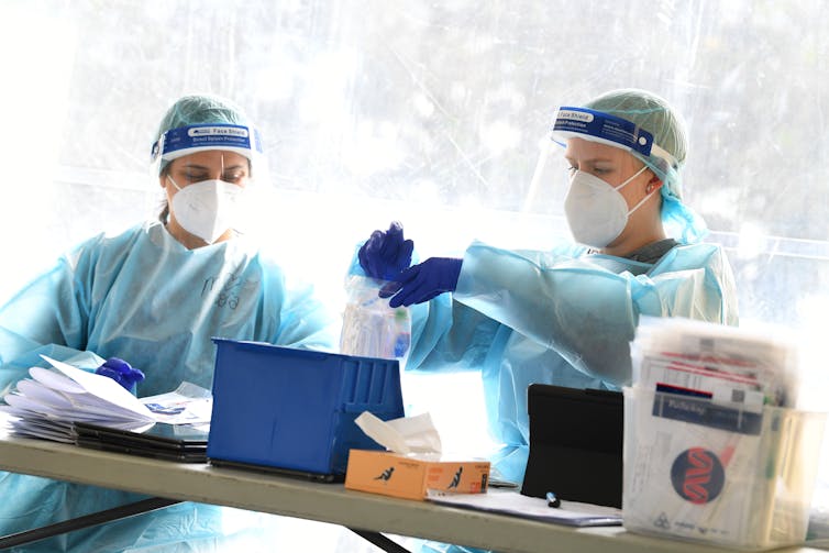 Two health-care workers wearing PPE are processing test samples.