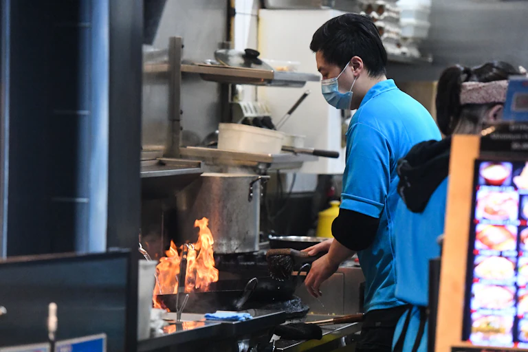 A man, wearing a mask, cooking in an industrial kitchen