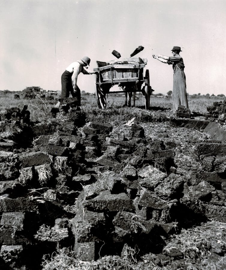 Two people load chunks of solid earth into a cart.