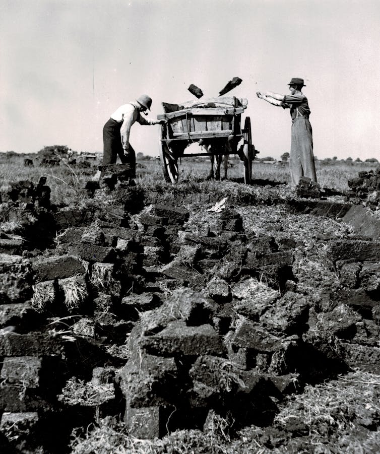Two people load chunks of solid earth into a cart.