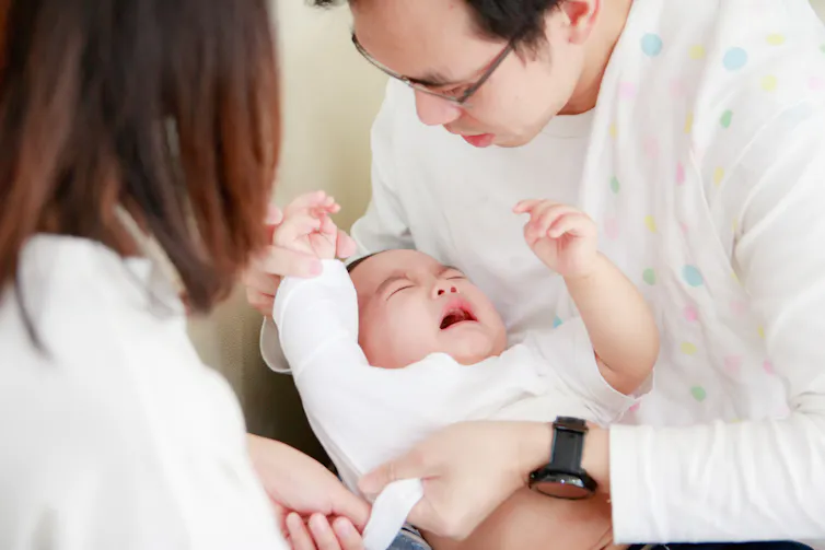 Two parents hold a crying baby.