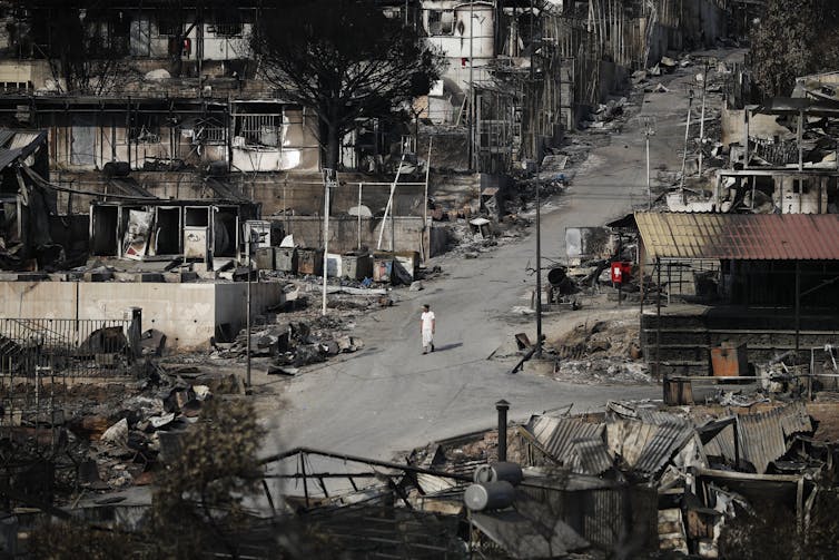 A man walks down a road surrounded by blackened out tents and shacks.