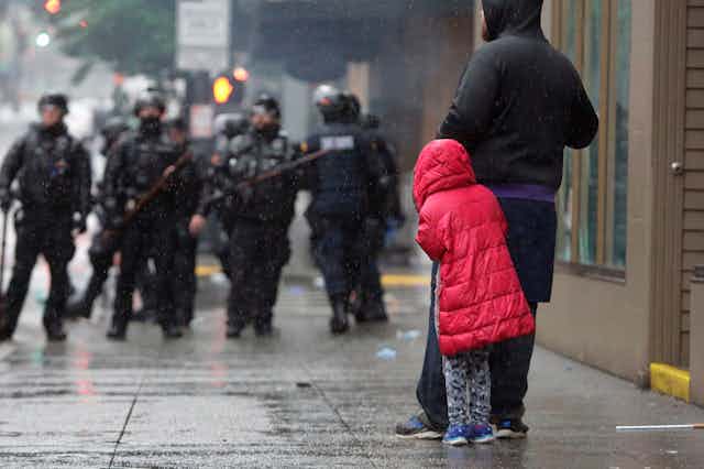 A girl cowers behind an adult in front of police in riot gear at a protest over the death of George Floyd.