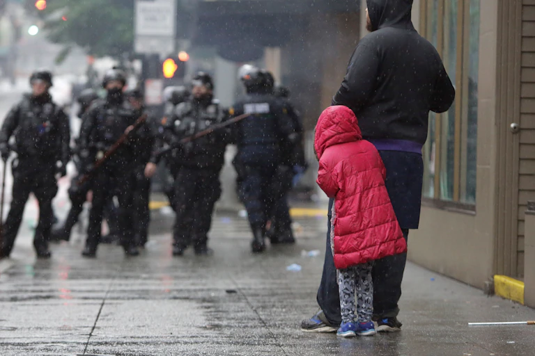 A girl cowers behind an adult in front of police in riot gear at a protest over the death of George Floyd.