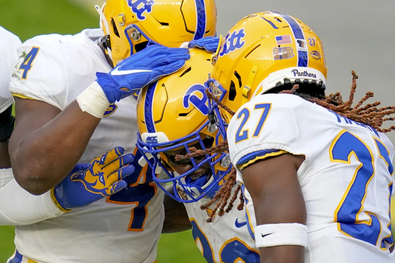 Three University of Pittsburgh football players celebrate a blocked punt.