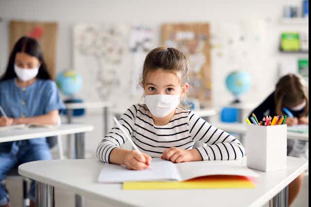 Schoolchildren wearing face masks sit at their socially-distanced desks.