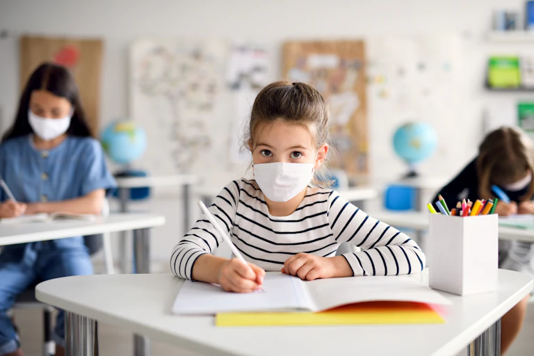 Schoolchildren wearing face masks sit at their socially-distanced desks.