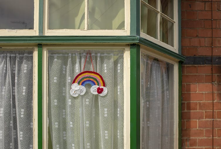 A crocheted rainbow hangs in a window.