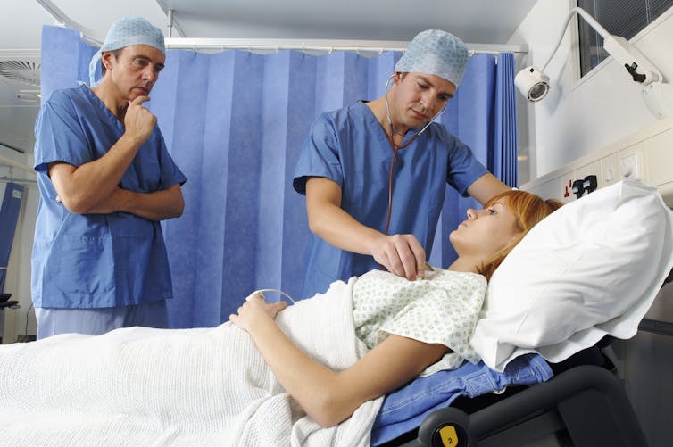 Two doctors stand next to a patient in a hospital bed.