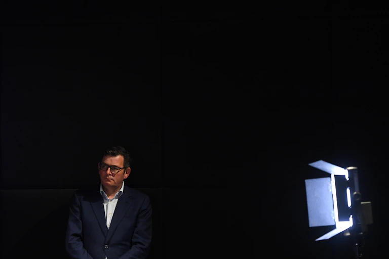 Daniel Andrews standing off stage at his press conference, next to a stage light