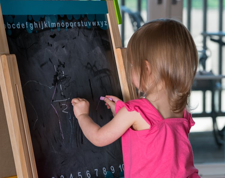 A young girl writing on a blackboard with both hands at the same time.