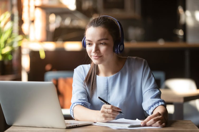 Woman with headphones on holding pen looking at laptop screen