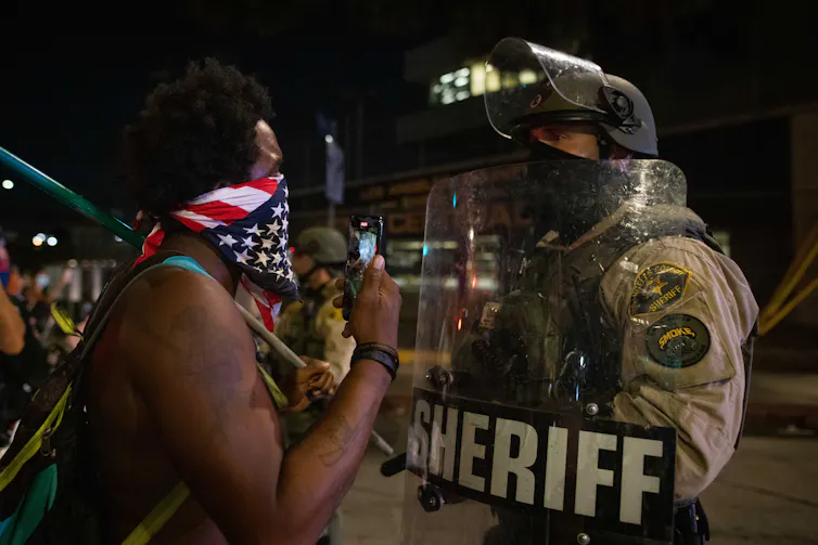 Man with American flag bandana talks to policeman with shield marked sheriff