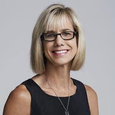 A woman with blonde hair and glasses smiles