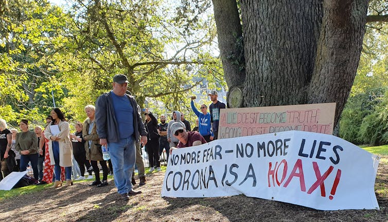 A man stands beside a sign that reads: 'No more fear – no more lies coronavirus is a hoax!'