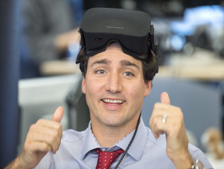 Justin Trudeau wears VR goggles on his head and gives a thumbs up.