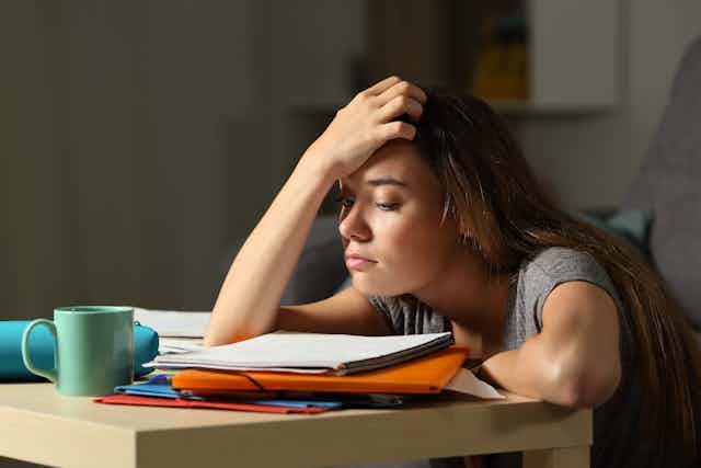 Girl sitting at study desk, looking tired.