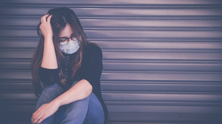 A young woman in a mask looks down.