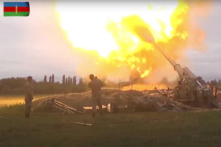 An artillery gun firing with two men standing next to it.