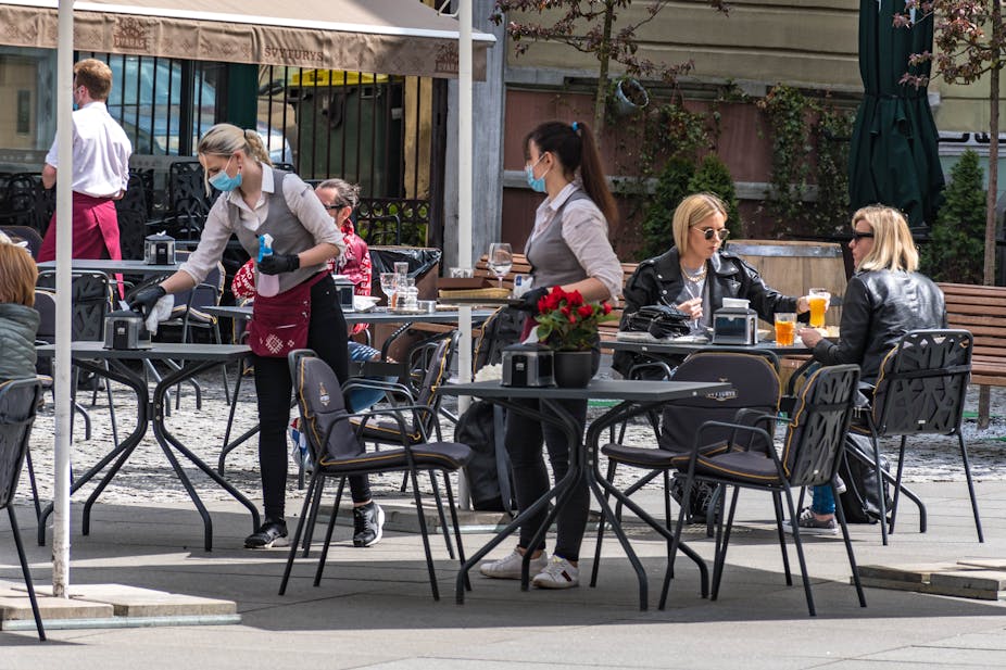 Waitresses with a mask and gloves disinfecting the table of an outdoor cafe.