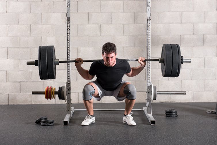 Man performs a squat with a barbell on his back.