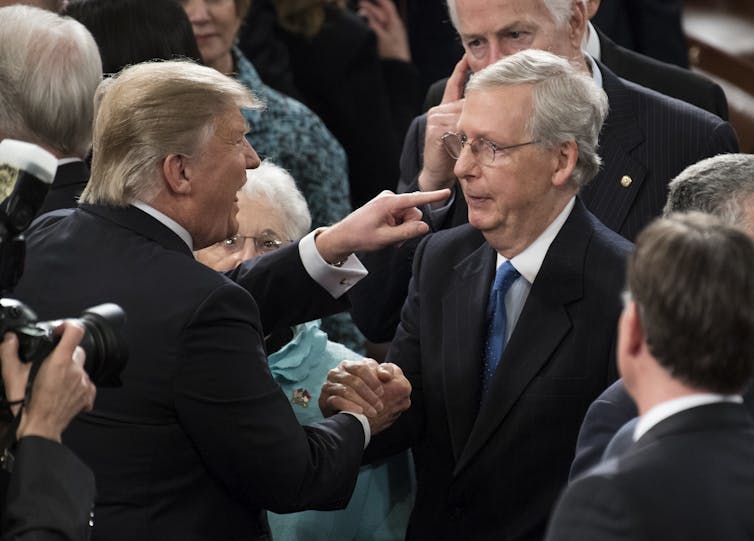 Trump points at McConnell in a crowd while shaking his hand
