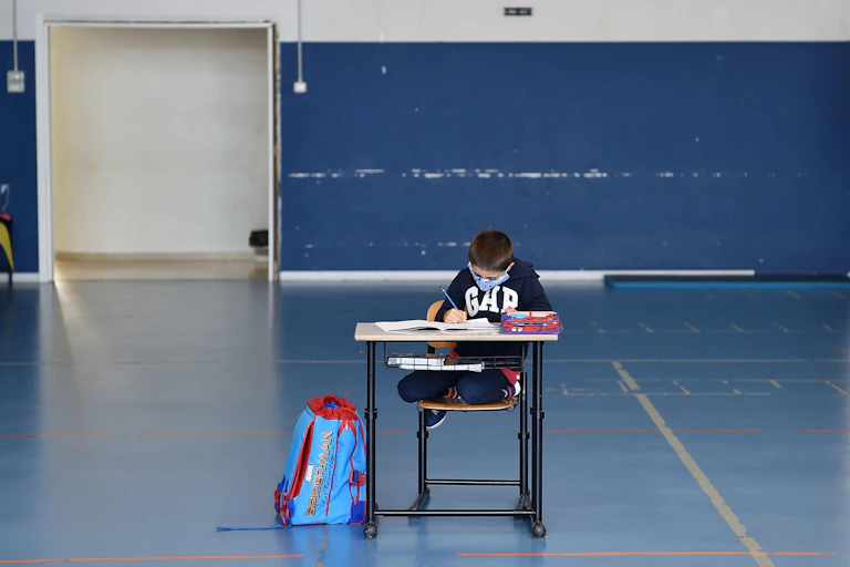Child alone at school desk wearing mask