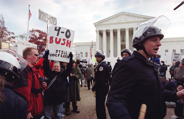 Protesters hold pro-Bush signs while police do crowd control, with Supreme Court in the background