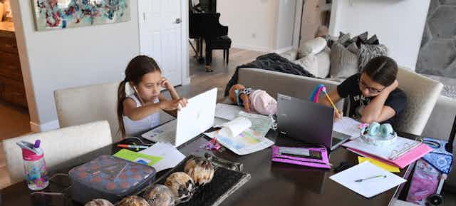 Two sisters do remote education at their dining room table.