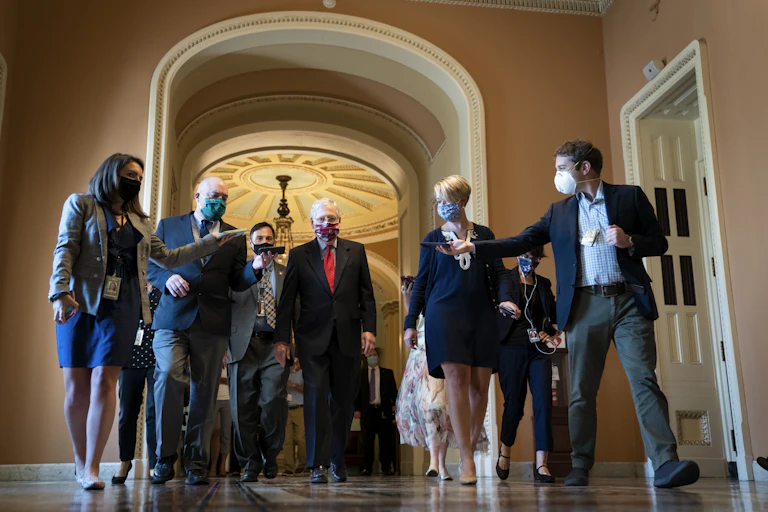 McConnell in a mask, walking through the Capitol surrounded by reporters recording him on cell phones