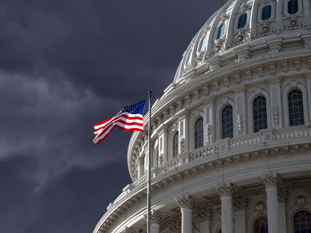 The US Capitol, with stormy skies and an American flag