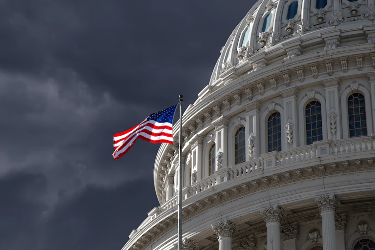 The US Capitol, with stormy skies and an American flag