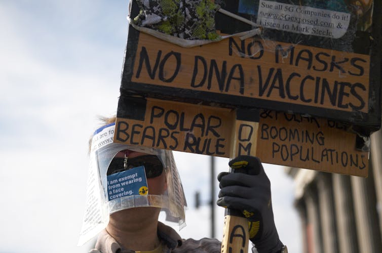 A person holding a sign including the words no masks, no DNA vaccines