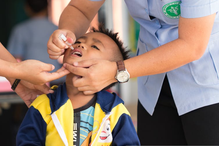 A health worker drops an oral polio vaccine into a child's mouth.