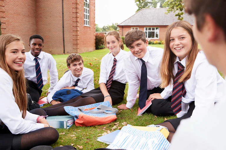 Private school students in uniform sitting on a school lawn.