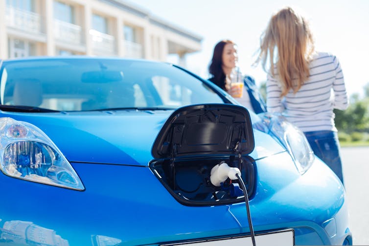 Two women standing next to an electric car.