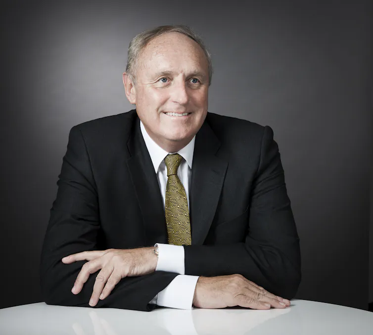 Head and shoulders shot of a middle-aged man in a suit and tie sitting at desk with his arms crossed.