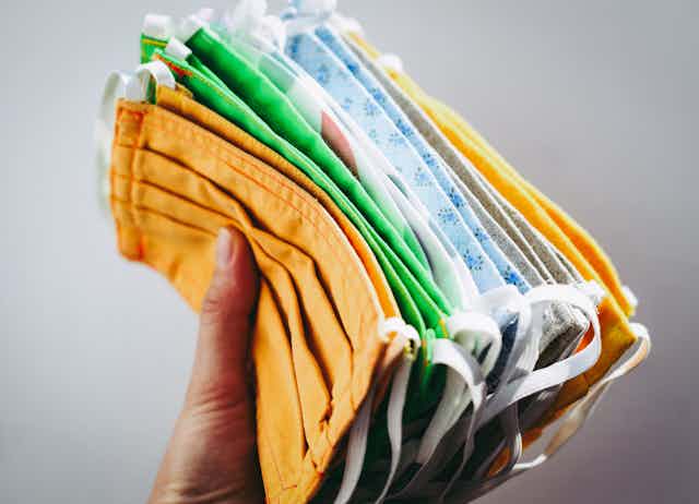 A hand holding a stack of cloth face masks in different colours: yellow, green and blue.
