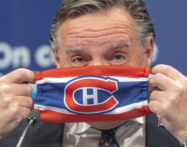 Québec Premier François Legault holds a face mask with the Montréal Canadiens logo in front of his face as he puts it on.