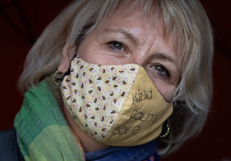Dr. Bonnie Henry wearing a cloth mask featuring bees and embroidered with the words 'kind calm safe'