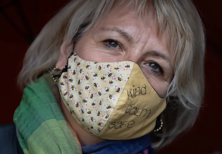 Dr. Bonnie Henry wearing a cloth mask featuring bees and embroidered with the words 'kind calm safe'