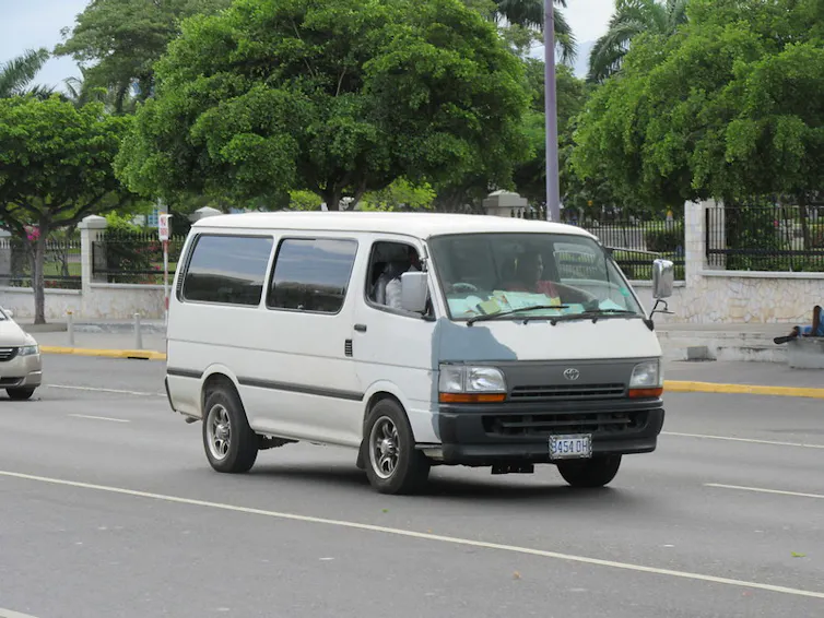 An old, white white Toyota minibus on a public road.
