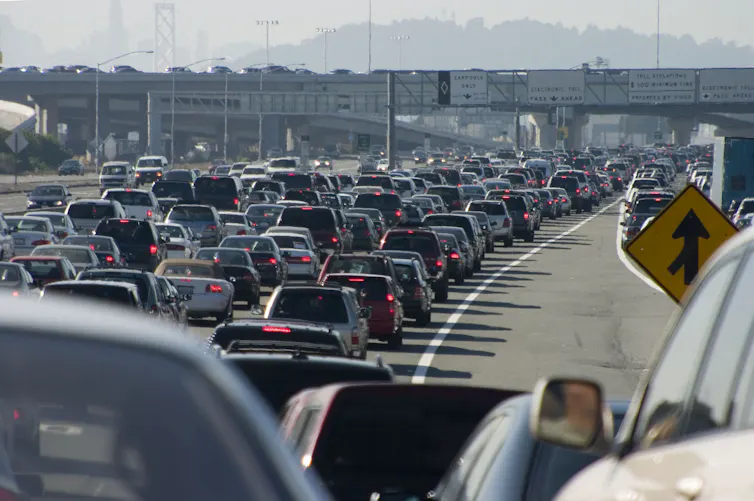 A traffic jam of cars with a bridge running over the road in the distance.