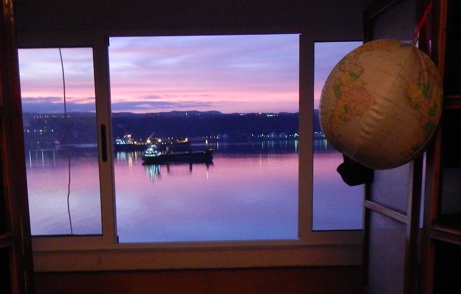 A look through a window shows the sunset reflected in water as a ship sails by