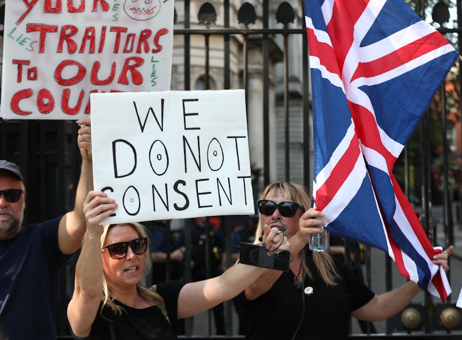A woman holding a sign reading 'we do not consent'. 